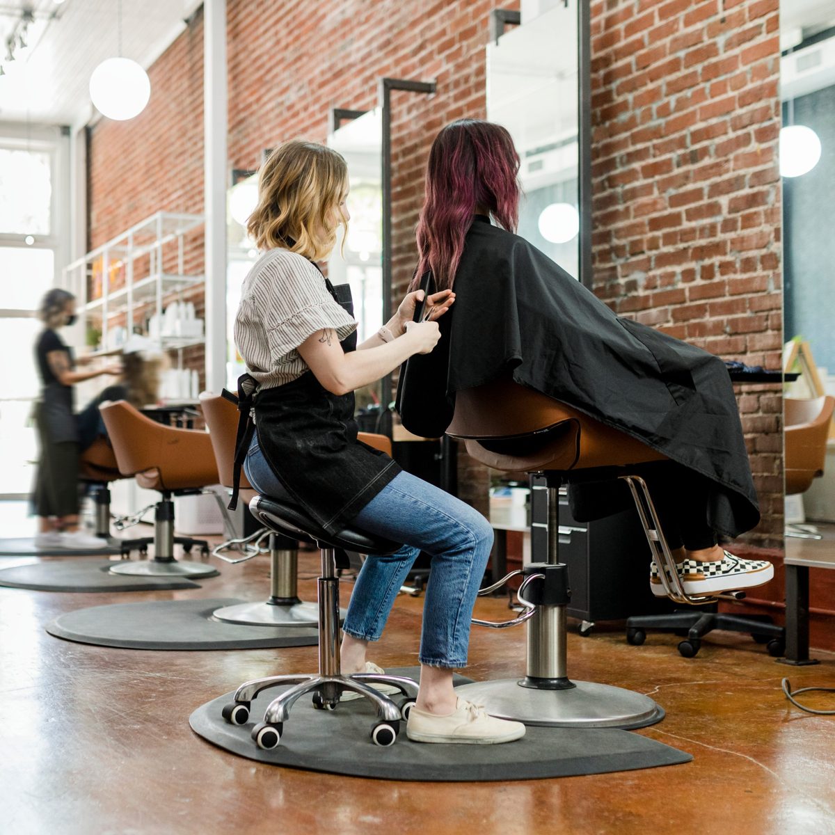Kapper aan het werk in een kapsalon met collega's op de achtergrond